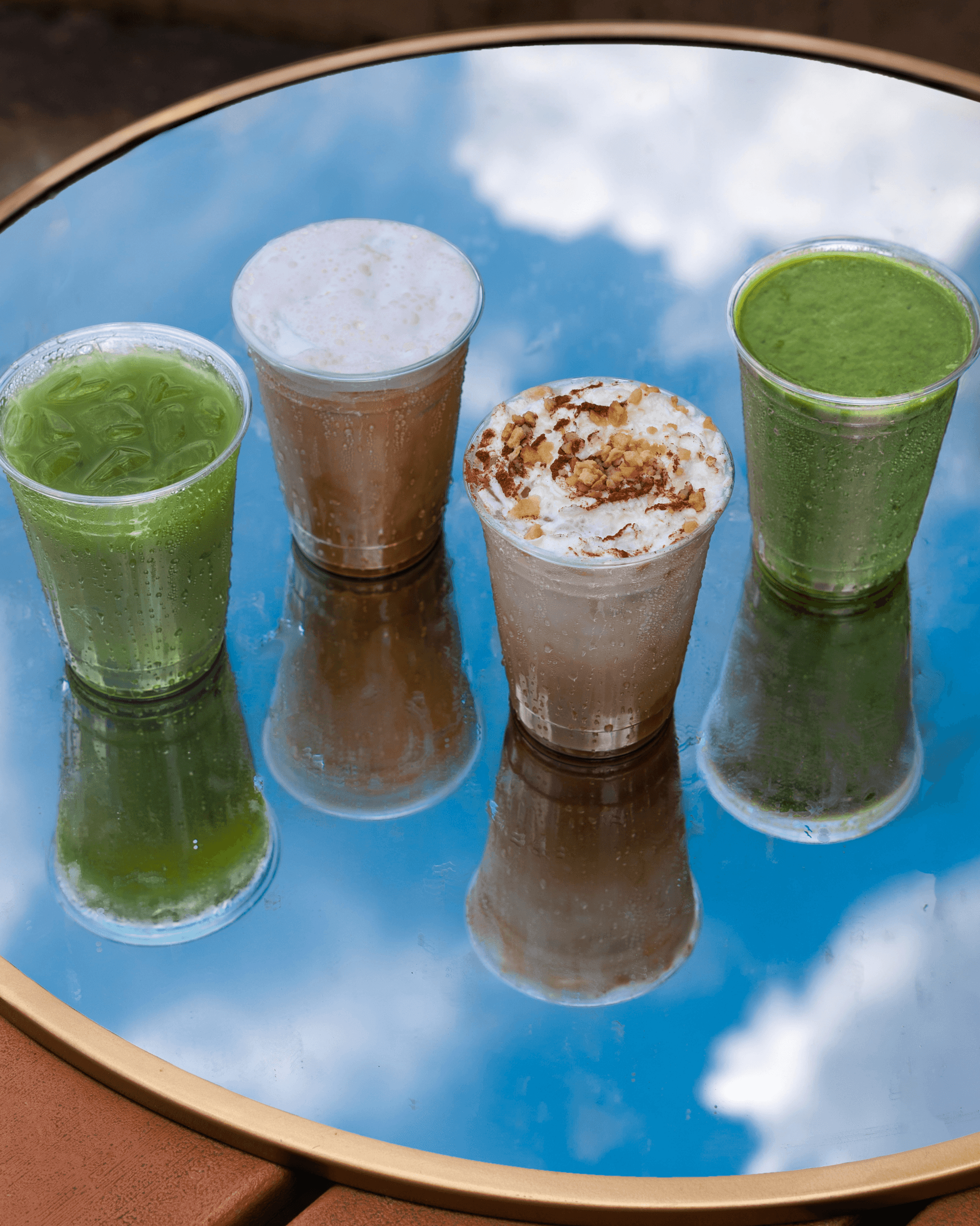 4 drinks sitting on a mirror with the sky being reflected