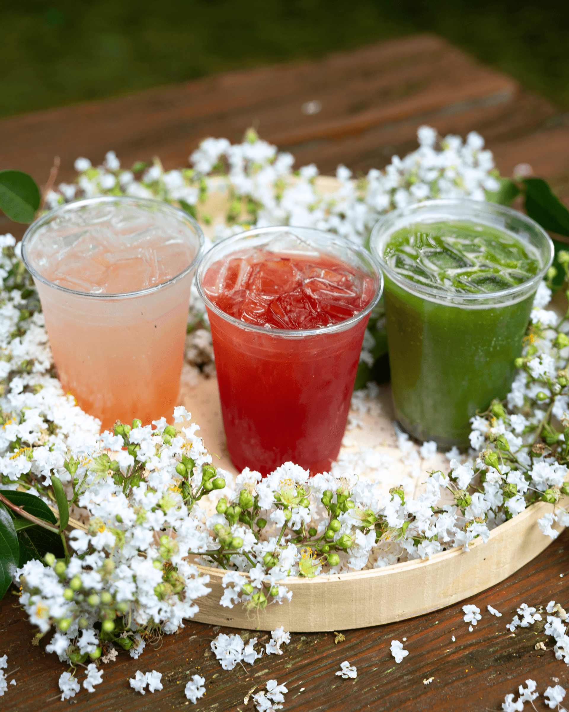 three drinks sitting on a table surrounded by flowers.